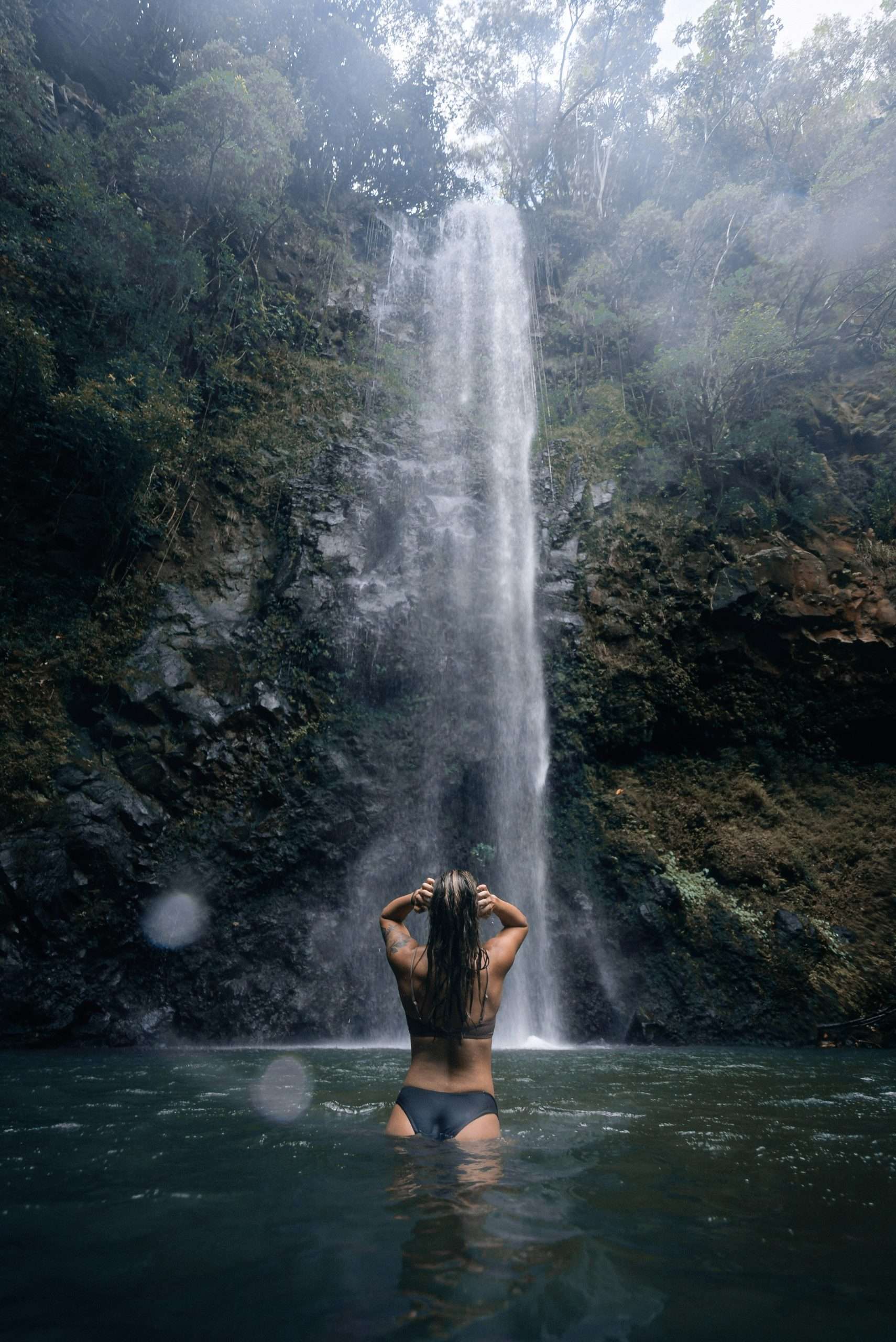 Woman swimming facing a dramatic jungle waterfall.